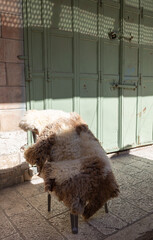 Fluffy sheepskin rug draped over a chair in front of a vintage green metal door © Oleg