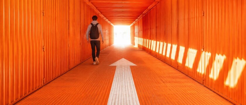 Person walking down an orange tunnel with a large white arrow on the floor