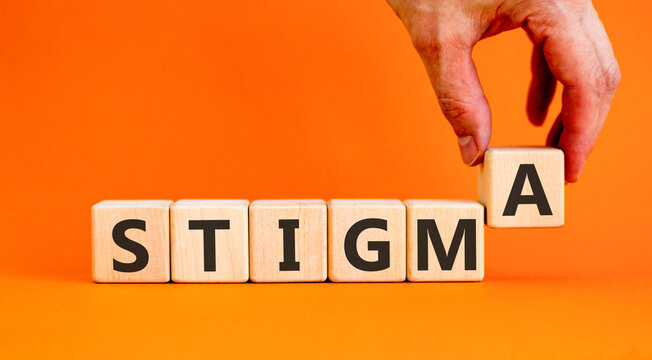 Stigma word symbol. Concept word Stigma on beautiful wooden blocks. Beautiful orange background. Psychologist's hand. Business psychological stigma word concept. Copy space.