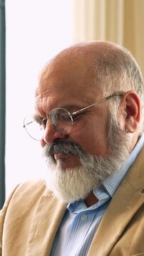 Indian Asian elderly businessman with a beard, dressed in a suit, seated in a chair, using a laptop to work,  relax between work  in a modern office