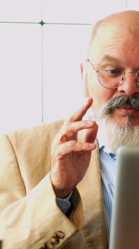 Indian Asian matured elderly businessman with a beard, dressed in a suit, seated in a chair in a modern office, using a laptop for video conferencing, for communication to discuss important business 