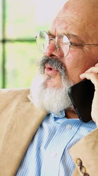 Indian Asian elderly businessman with a beard, wearing a suit, sitting in a chair, using a laptop and talking on the phone with a smile,  listening and explaining business matters 