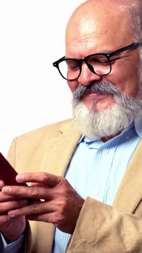 An Indian Asian senior businessman with a beard is standing against a white background, holding a smart phone happily typing a message and smiling
