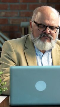Indian Asian elderly businessman with a beard, dressed in a suit, sitting in a modern office setup, using a laptop while counting Indian currency notes 