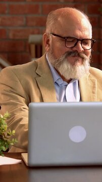 Indian Asian elderly businessman with a beard, dressed in a suit, sitting in a modern office, using a debit or credit card to make online purchases through a laptop
