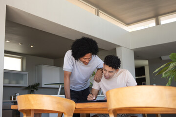 Fototapeta premium African American men friends leaning over table in kitchen writing on dark tablet casual tshirts