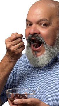 An Indian Asian elderly businessman with a beard is secretly enjoying a bowl of delicious gulabjamun