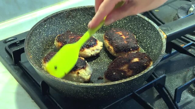 A young woman is frying chicken patties in a pan for dinner.