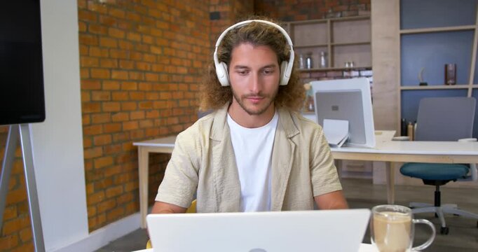 Man wearing headset working on laptop in brick wall office reaching and sipping mug refocusing