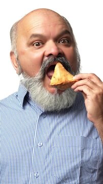 Indian Asian elderly gentleman with a beard  enjoys a samosa secretely ,showing love for Indian snacks