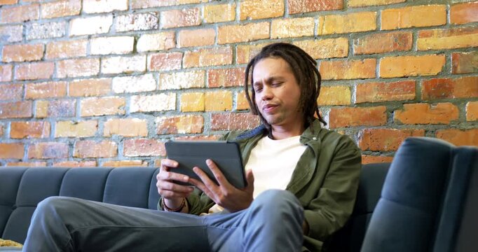 African American man shifting on dark blue sofa, reacting to confusing tablet notification