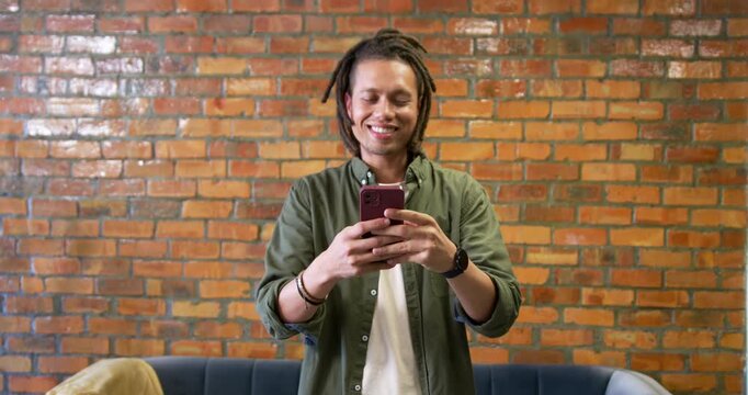 Dreadlocked man seeing message on red phone, reacting with smile and fist pump in lounge