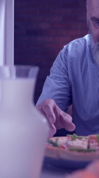 Indian Asian senior businessman with a white beard quietly opening the fridge in the middle of the night, eating a slice of pizza secretely