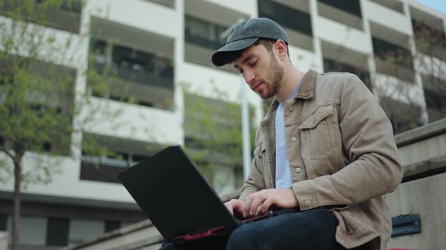 Student or young freelancer typing on laptop, working remotely outdoors in city