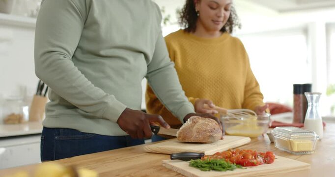 Starting meal prep, couple slicing roast on wooden cutting board, whisking eggs in glass bowl