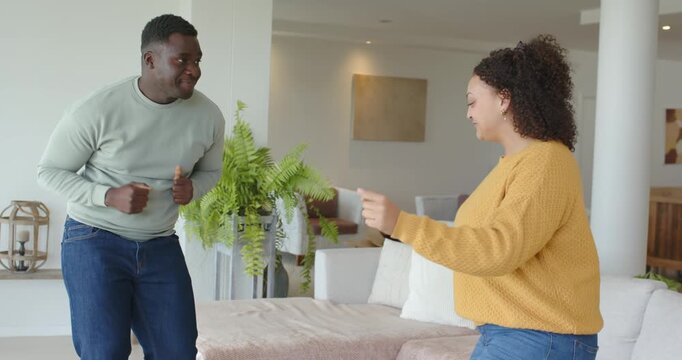 African American couple playfully dancing at home near fern, woman increasing energy, man mirroring