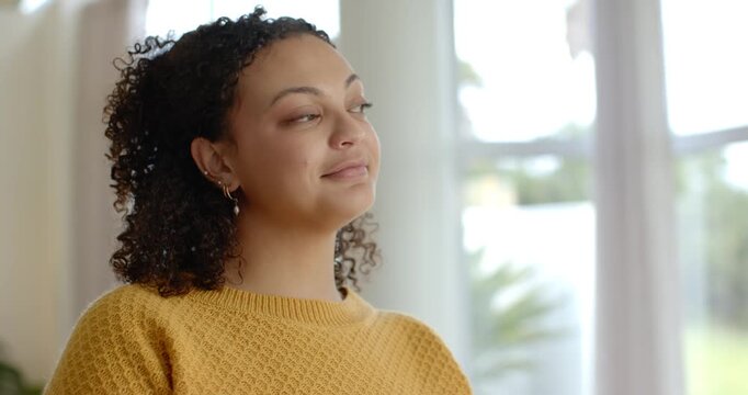 African American woman gazing out window, sighing, smiling and laughing at home in yellow sweater