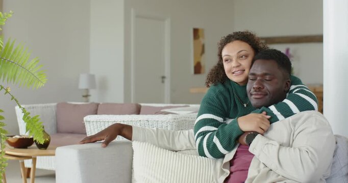 African American couple cuddling as woman leaning, wrapping arms around man on sofa for comfort