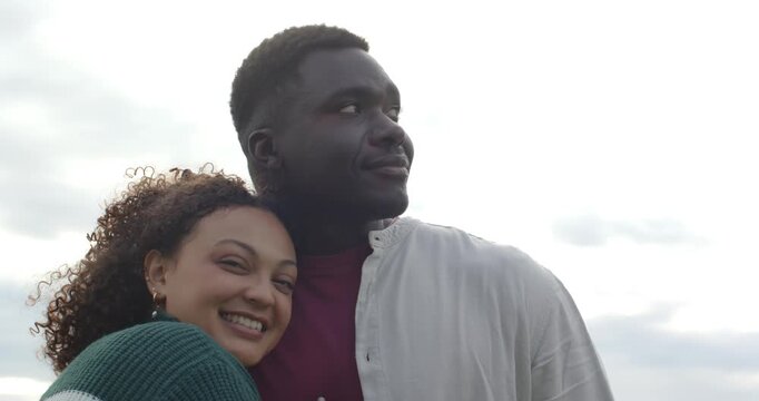 African American couple under cloudy sky, woman wearing green sweater leaning in, showing affection