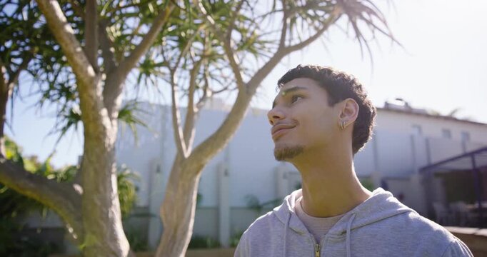 African American man 20s by palm tree in yard tilting toward sun, facing camera, acknowledging