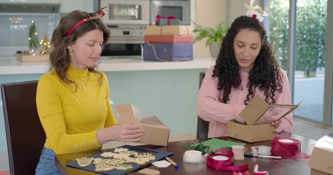 Diverse women friends at dining table opening boxes assembling clear window boxes for holiday gifts