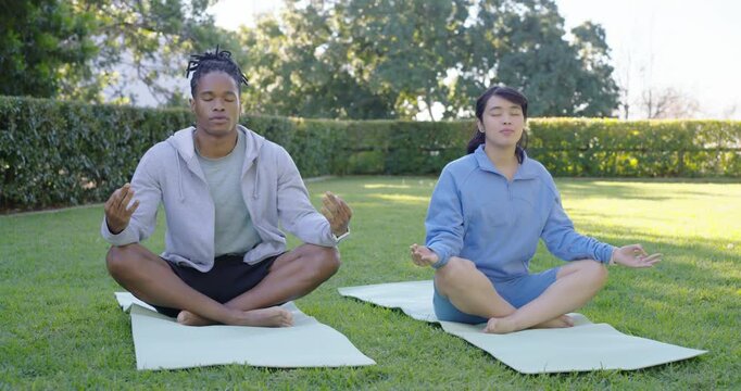 Couple settling onto light-green yoga mats, holding meditation mudra while calming breath together