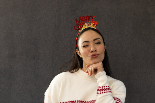 Adult female posing winking puckering lips in studio wearing sweater Merry Xmas headband gold hoops