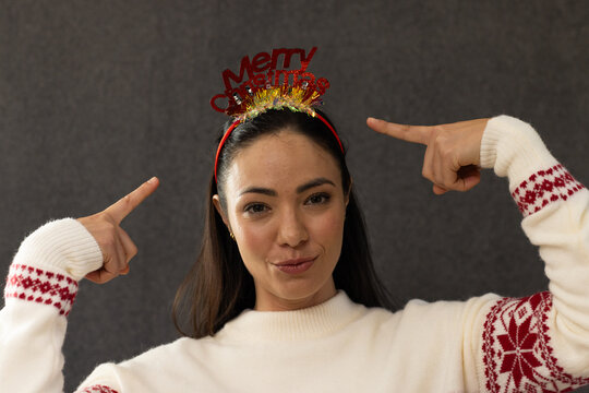 Woman pointing to red Merry Christmas headband while posing in studio wearing Nordic sweater