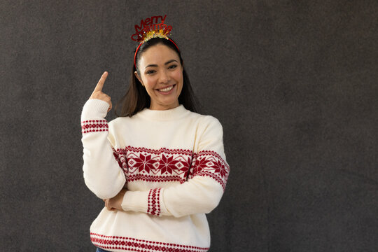 Adult woman posing before dark backdrop in sweater smiling, pointing at headband with gold tinsel