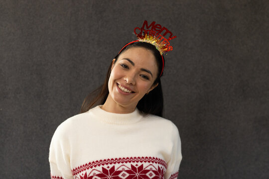 Adult woman smiling tilting left wearing Merry tinsel headband white Nordic sweater studs in studio