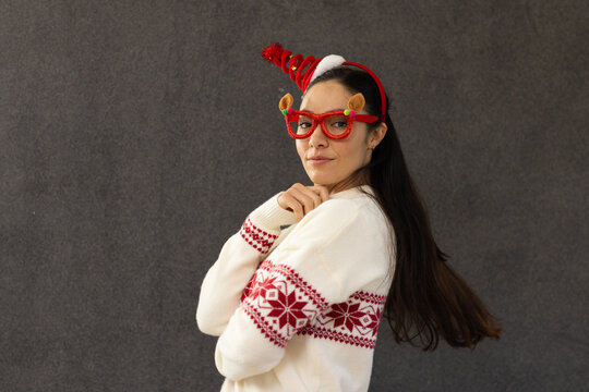 Asian woman posing over left shoulder in studio wearing Nordic sweater, reindeer glasses, headband