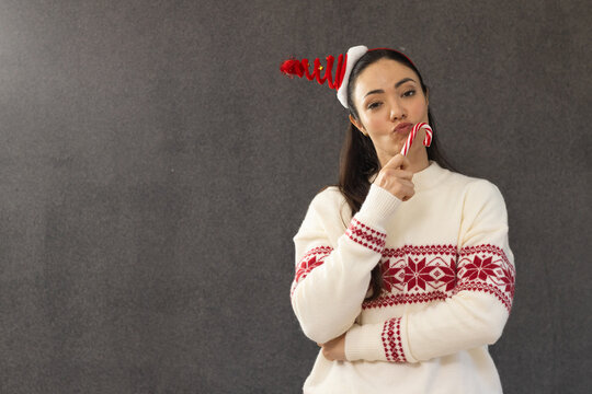 Adult female posing right against dark gray wall, holding candy cane, in Nordic sweater, copy space