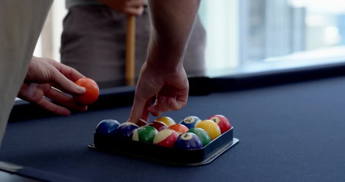 Male friends racking balls with metal rack on pool table, smiling and holding cue preparing game