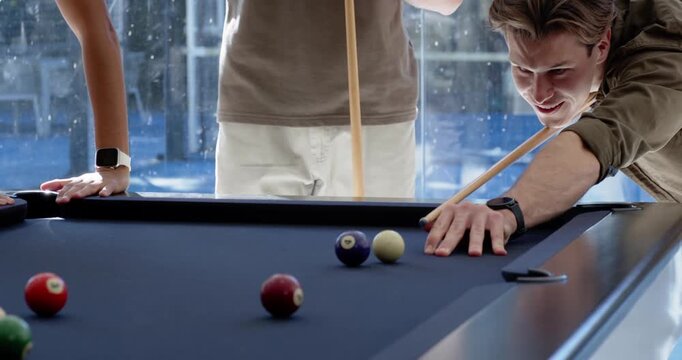 Male friends leaning by blue-felt pool table in lounge, shooter aiming, striking cue ball for fun