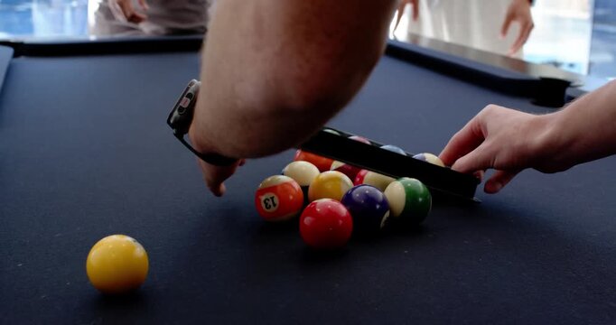 Diverse male friends placing and adjusting rack over balls on black felt table preparing break shot