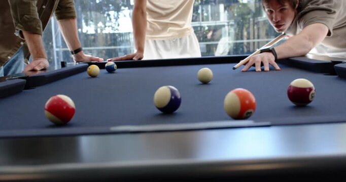 Three men watching shooter breaking on blue-felt table, trying to pocket numbered balls, copy space