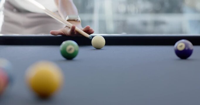Diverse male players pulling cue, striking white ball at pool table toward right pocket to sink