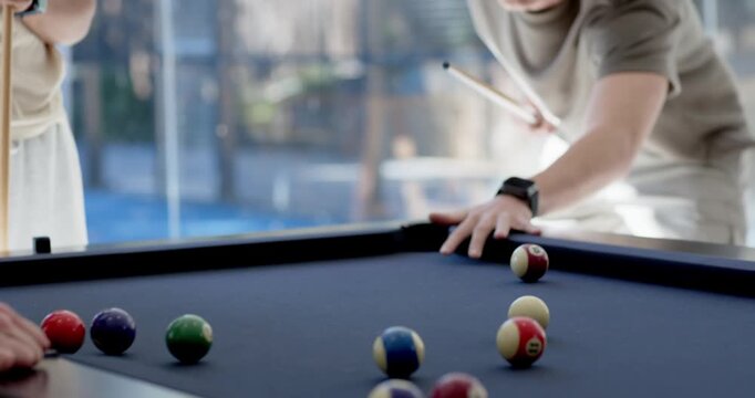 Adult male friends playing pool main player taking shot lining and striking cue at scattered balls