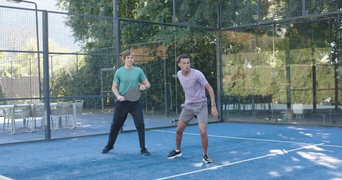 Two male friends leaping driving returning lob with paddles on court, keeping rally then laughing