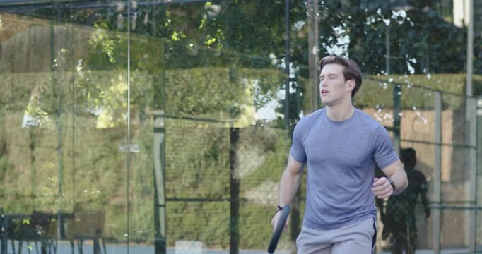 Diverse male players in sportswear intercepting ball, striking paddles on glass court training