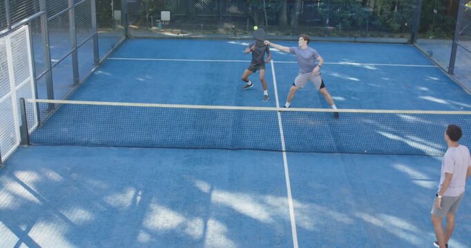 Four men starting rally on blue court lower-right swinging paddle sending ball forcing volley