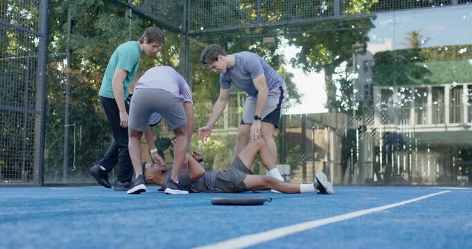 Diverse men in sportswear helping fallen player on blue court kneeling lifting him near black pouch