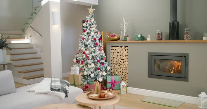 Camera is panning and zooming to flocked Christmas tree as fireplace is flickering, showing gifts