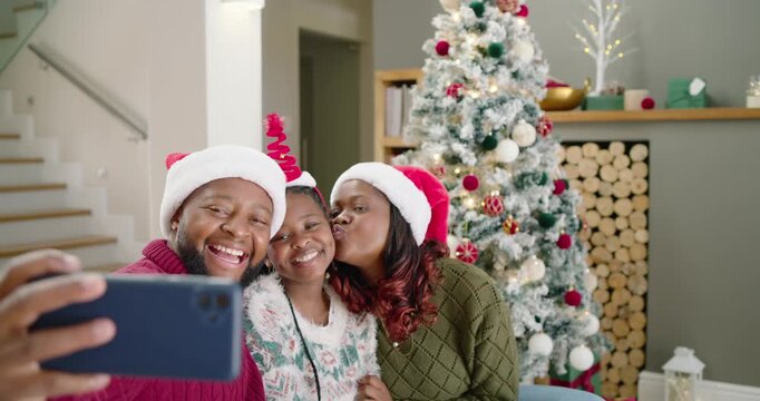 African family father holding smartphone, posing to capture Christmas memories on couch near tree