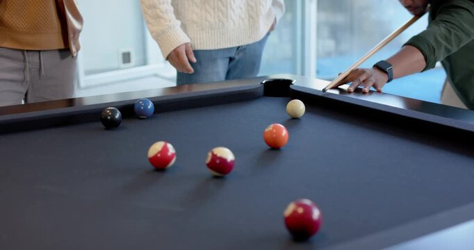 Diverse male friends cheering African American man lining up, striking cue at home, sinking balls