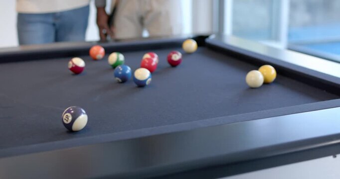Diverse men playing on pool table, cue hitting ball, jacketed man celebrating and hugging in lounge