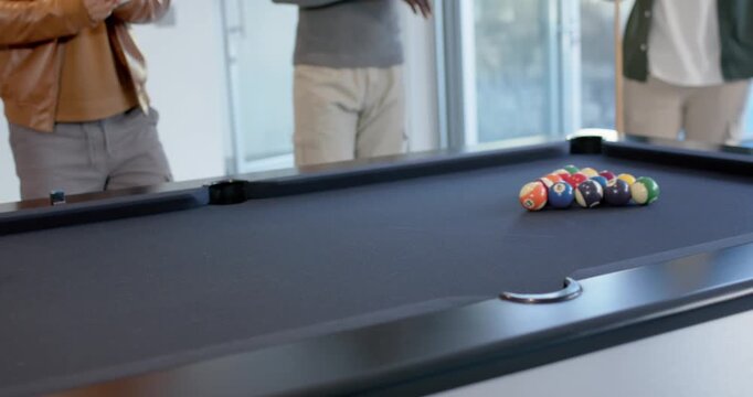 Diverse men in game-room at pool table player placing cue aligning ball breaking rack starting game