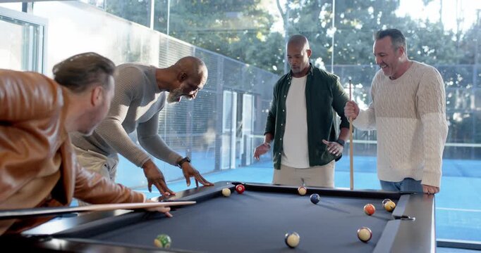 Diverse male friends watching shooter striking cue ball at pool table during friendly game