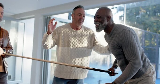 Diverse men at pool table playing with cues, cheering African American man lining-up, taking shot