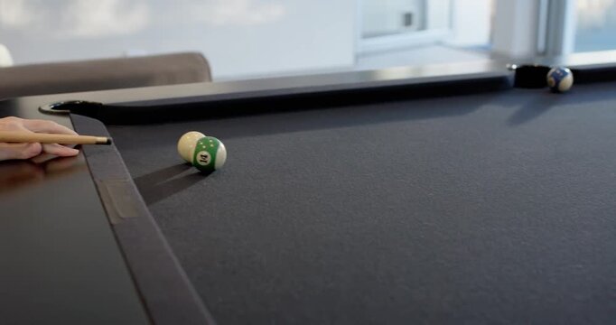Two male friends playing pool, shooter lining up and striking wooden cue, watching striped ball